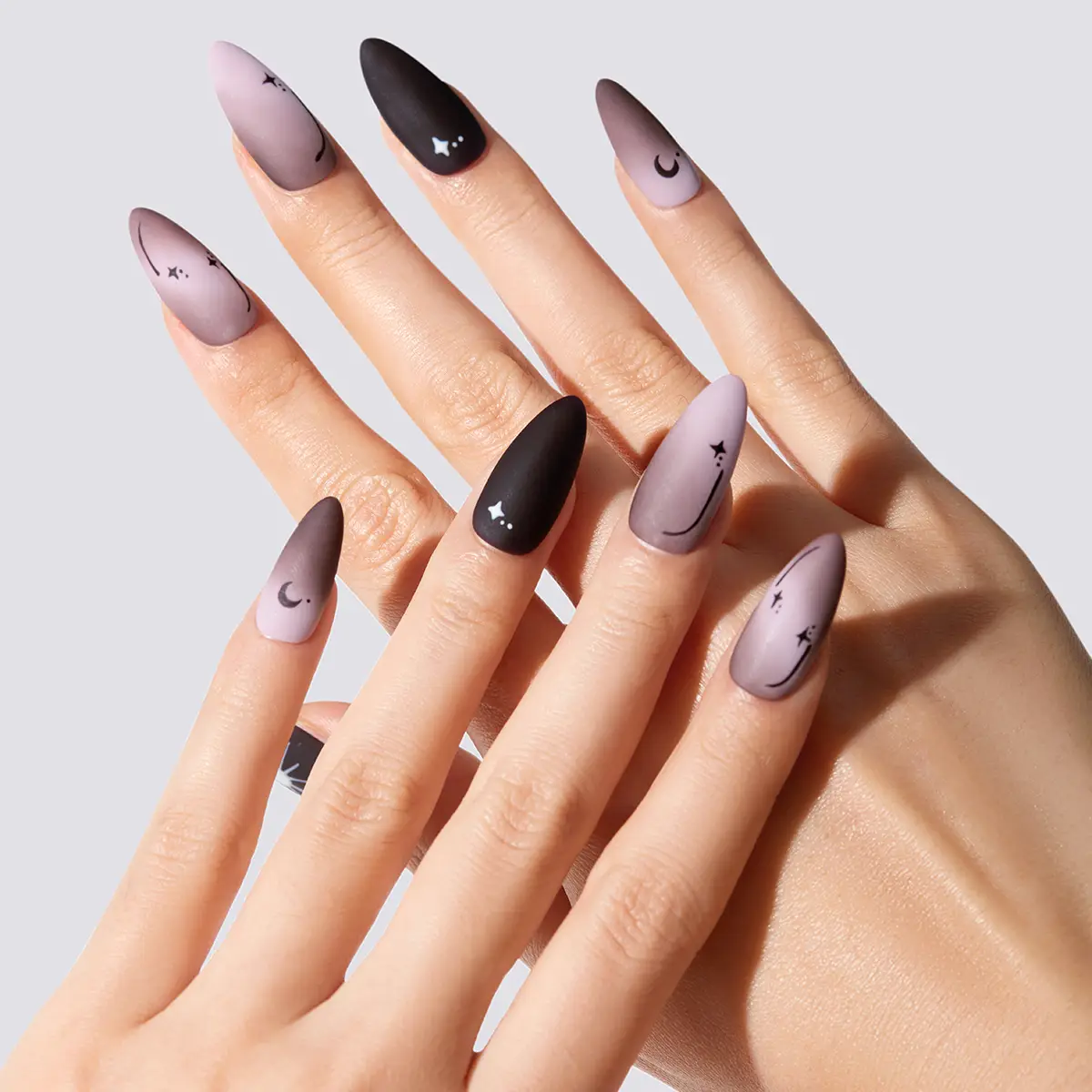 Mystic Tarot Handmade matte black and dusty rose ombre almond press-on nails with white hand-painted sun, moon, and star motifs, close-up detail